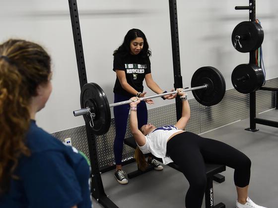 Photo of a woman helping another woman use a bench press.