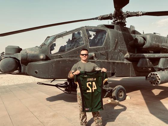 尼克·朱斯蒂(Nick Giusti)在一架驻扎在叙利亚的直升机前举起金沙js6038(McDaniel)足球球衣.