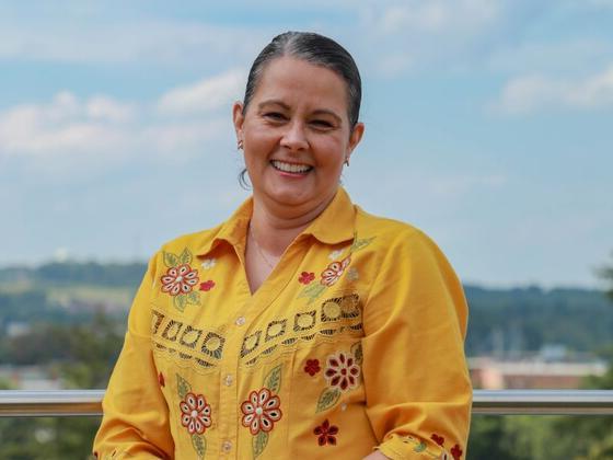 Photo of a woman standing on an overlook wearing a yellow flowered shirt with horizon behind her.