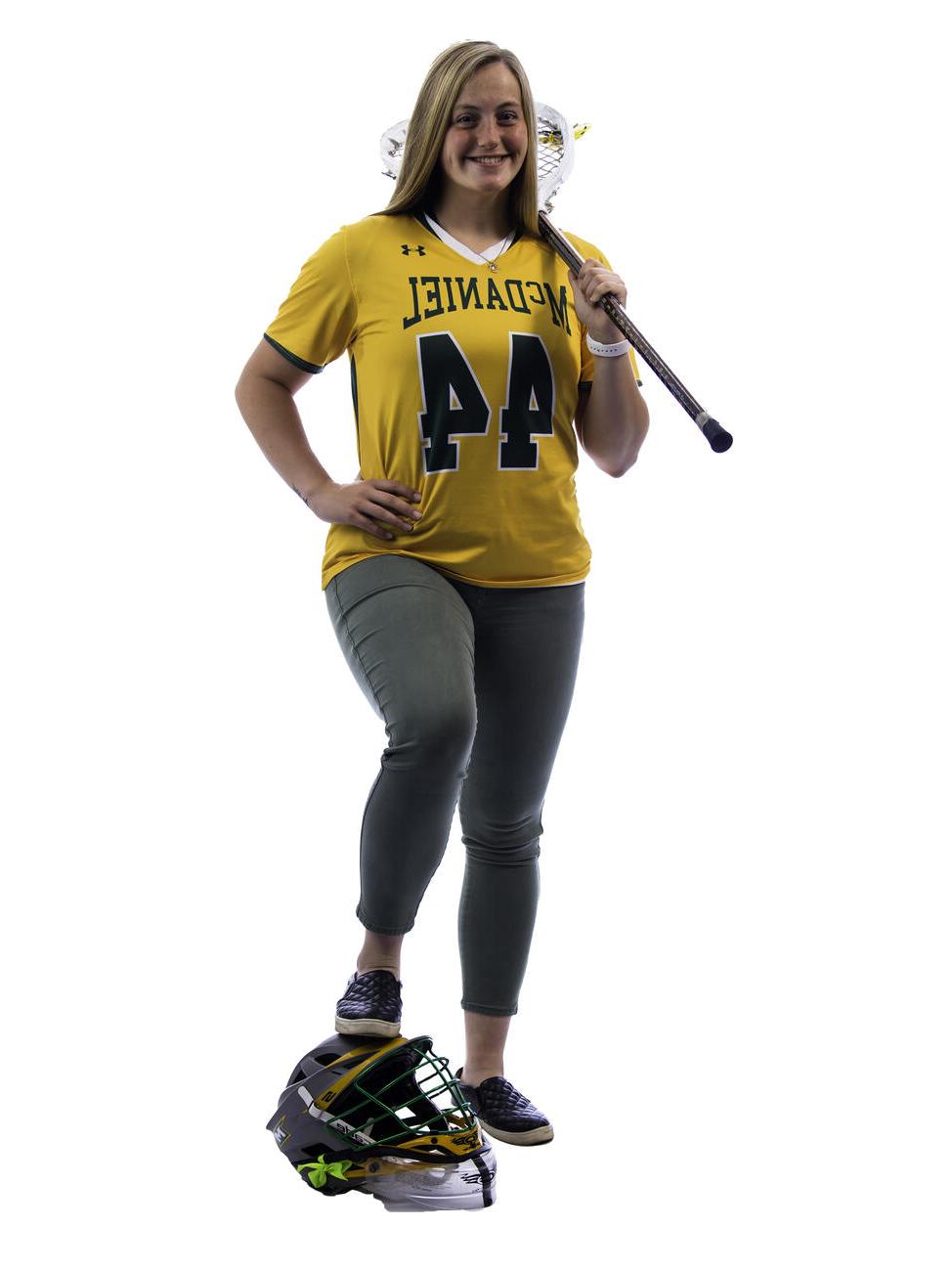 汉娜·米勒的姿势与长曲棍球棒在她的肩膀和她的脚上的头盔.