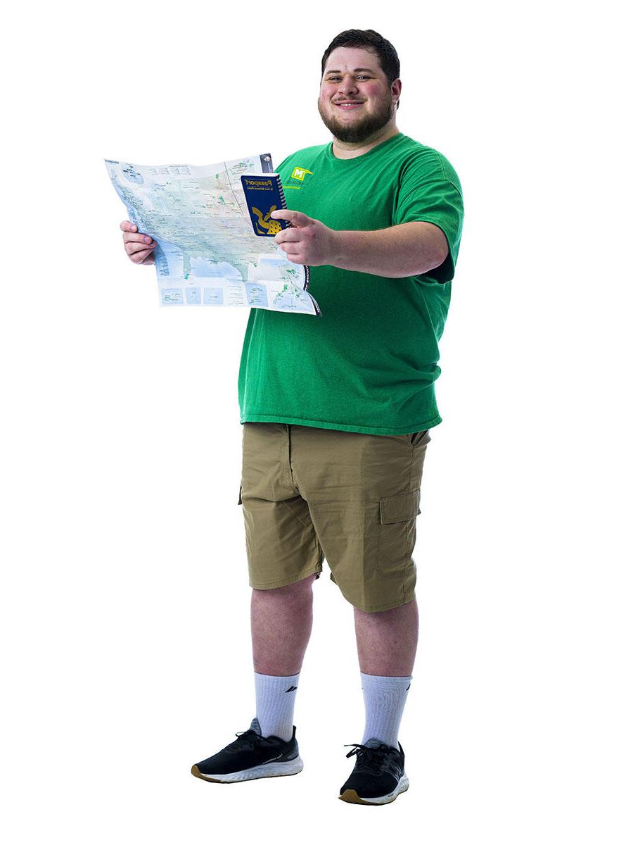 一名身穿绿色衬衫的学生站在白色背景前，手里拿着地图.