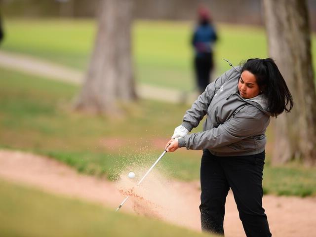 Photo of a student hitting a golf ball and kicking up dirt.