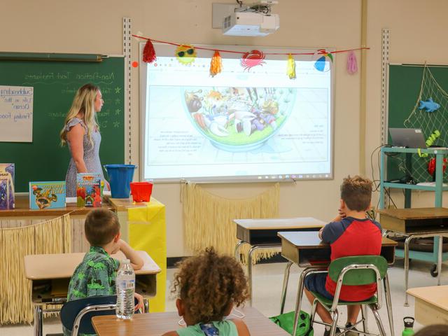 图为，一名女教师站在教室前面，看着投影仪上的影像.