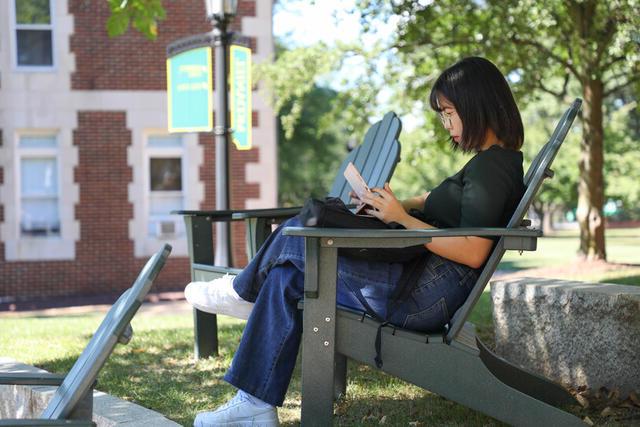 一名学生在校园里坐在一把绿色的阿迪朗达克椅子上读书.