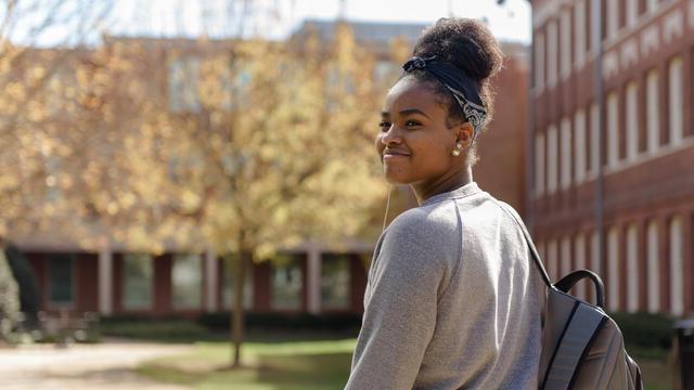 A student on campus looks back over her shoulder while smiling.